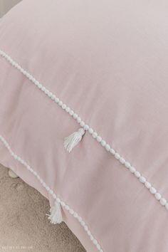 a pink pillow with white tassels and beads on the edges is sitting on a beige carpet