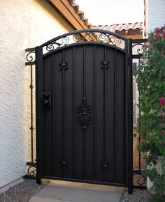 a black gate with an iron design on the top and bottom, in front of a house