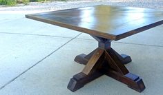 a square wooden table sitting on top of a cement floor next to a sidewalk and grass