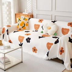 a living room with a white couch covered in an orange and black flowered cover