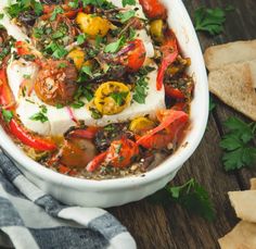 a white bowl filled with lots of food on top of a wooden table next to bread