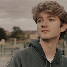 a young man standing in front of a fence with his eyes closed and looking off into the distance