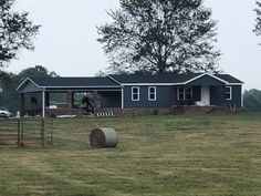 a farm house with hay bales in the foreground and a horse grazing on the other side