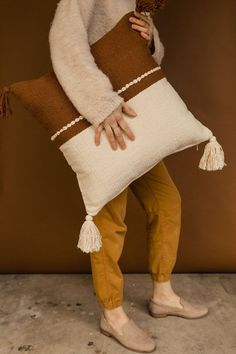 a woman is holding a pillow that has been knitted with yarn and tassels