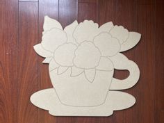 a paper cut out of a coffee cup with flowers on the front and side, sitting on a wood floor