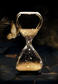 an hourglass with gold glitter and a butterfly on it's side, against a black background