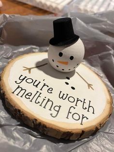 a small snowman sitting on top of a piece of wood that says, you're worth melting for