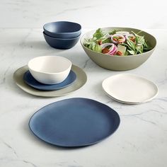 three bowls and two plates on a marble countertop with salad in the middle, one bowl is blue