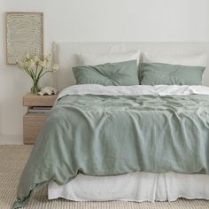 a bed with green linens and pillows in a white walled room next to a plant