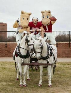 two people riding on the back of a horse drawn carriage with three mascots standing behind them