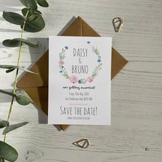 a wedding save the date card on top of a brown envelope with greenery around it