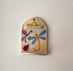 a ceramic plaque with dragonflies and ladybugs painted on it's side