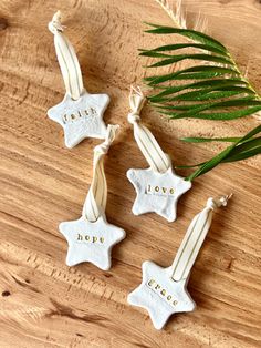 three white ceramic stars with the word love hanging from them on a wooden table next to a plant