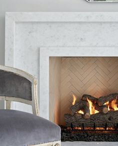 a white fireplace with a mirror above it and a chair in front of the fire