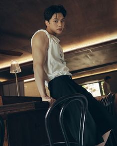 a young man sitting on top of a chair next to a wooden table and lamp