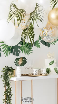 a table topped with lots of balloons and greenery next to a white counter top