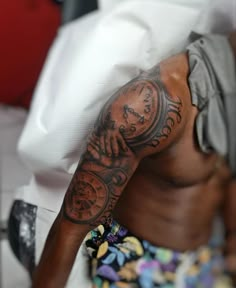 a man with a clock tattoo on his arm sitting in bed next to a pillow