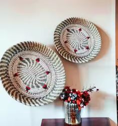 two woven baskets on a table with flowers in a vase next to it and the wall behind them