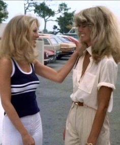 two women standing next to each other in a parking lot talking and smiling at each other