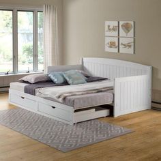 a white bed with two drawers underneath it in a bedroom next to a large window