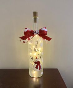 a lighted bottle with a snowman and red bow on it that says let it snow