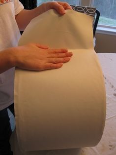 a person is making a pillow out of a roll of paper on a table with a window in the background