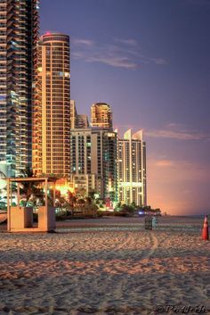 the city skyline is lit up at night on the beach in front of tall buildings