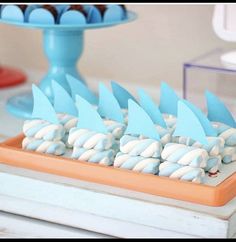 there are many blue and white desserts on the table with cupcakes in the shape of shark fin