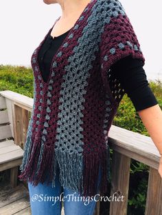 a woman wearing a crocheted shawl standing on a wooden bench