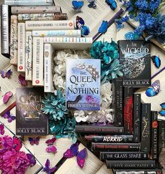 a pile of books sitting on top of a table next to purple and blue flowers