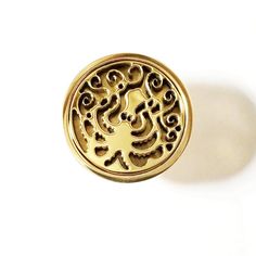 a gold button with an intricate design on the front and back side, against a white background