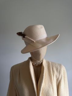 "This striking vintage hat features a face-framing brim; a soft, cream felt body; and an elegant, arching pheasant feather and wool \"bow.\"  Era: 1970s  Label: Peachfelt | 100% wool | Geo W Bollman and Co USA Pictured on a mannequin with a 21 inch head circumference About Geo W Bollman hat company from their website:  * Bollman Hat Company is the oldest hat maker in America, and among the world's oldest because of a stewardship culture and a continuous focus on our innovation, unsurpassed quali Classic Beige Fedora Felt Hat, Beige Cloche Hat With Curved Brim For Fall, Elegant Fedora With Curved Brim For Fall, Elegant Curved Brim Fedora For Fall, Elegant Fall Fedora With Curved Brim, Fitted Beige Wide Brim Fedora, Classic Cream Fedora For Winter, Winter Feathered Flat Brim Felt Hat, Classic Beige Cloche Hat With Flat Brim