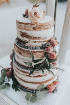 a three tiered cake with flowers and greenery on the top is sitting on a table