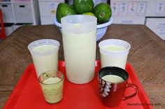 there are three cups on the tray with milk and limes in the background,