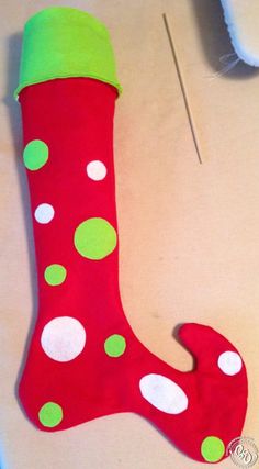 a red and green sock with white dots on it next to a sewing needle in the shape of a christmas stocking