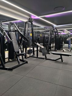 an empty gym with equipment and people in the background at night or early evening time