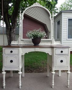 a white vanity with a mirror and flower pot on the top, sitting in front of a house