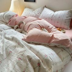 an unmade bed with pink and white comforter on top of it next to a lamp