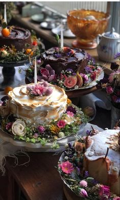 a table topped with lots of cakes covered in frosting and flowery toppings