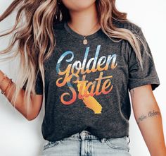 Embrace the spirit of California with our Golden State California Graphic Tee. This unique t-shirt features a sunset-themed design with the iconic "Golden State" typography, giving it a vintage and stylish look. Perfect for both men and women, it's an ideal choice for anyone who loves the West Coast. Wear this tee to showcase your love for California and its laid-back vibe. Great for casual outings, vacations, or simply lounging around in comfort. Available in various sizes to suit your fit. At BOP Prints, we believe in delivering both style and comfort with every design 👕✨. Our shirts are crafted using the high-quality Bella + Canvas 3001 tees, known for their superior softness, lightweight feel, and long-lasting durability 🧵👌. Whether you're looking for the perfect gift 🎁 or somethin California Graphic, West Coast Style, West Coast Fashion, Coast Style, Typography T Shirt, Typography Tshirt, Pride Tshirts, Golden State, Style Shirt