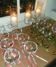 there are many wine glasses on the table with candles in front of them and some pink ribbons