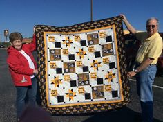 two people standing next to each other holding up a black and yellow quilt on the street