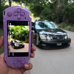 a person holding up a cell phone with a car on the street in front of them