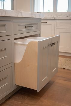 a white kitchen with gray cabinets and wooden drawers on the bottom cabinet is an empty dishwasher