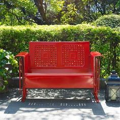 a red bench sitting in front of a bush and some bushes with lanterns on the ground