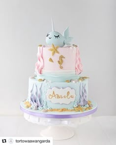 a three tiered cake decorated with an ocean theme and unicorn on the top layer