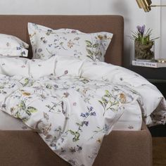 an unmade bed with white sheets and flowers on the comforter, next to a plant