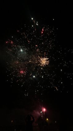 fireworks are lit up in the night sky with people standing on the sidewalk watching them