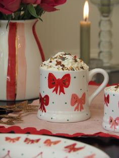 two coffee mugs with bows on them sitting on a table next to a candle