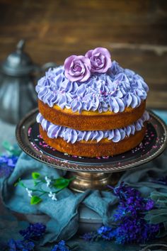 a three layer cake with purple frosting and flowers on top, sitting on a plate